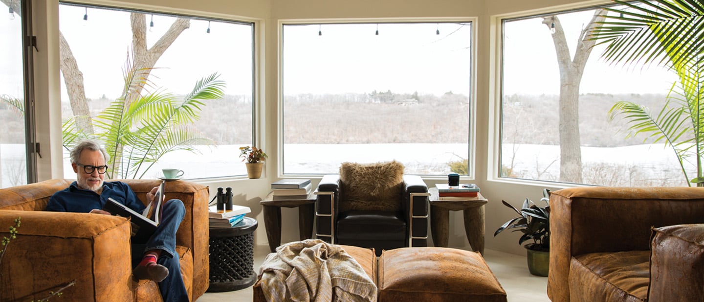 Man reading a book in his living room with Andersen 400 series casement & picture types of windows